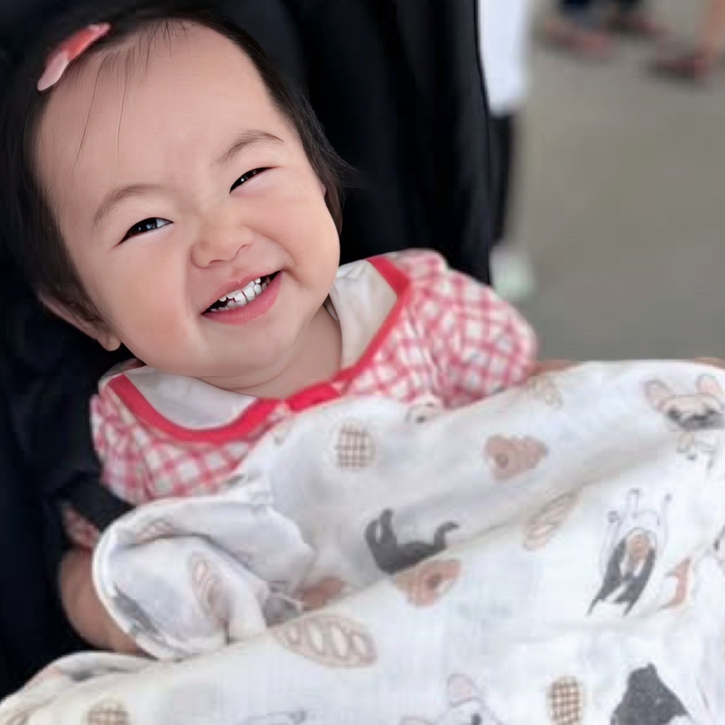 フレンチブルドッグ柄のガーゼのおくるみに包まれる笑顔の赤ちゃん